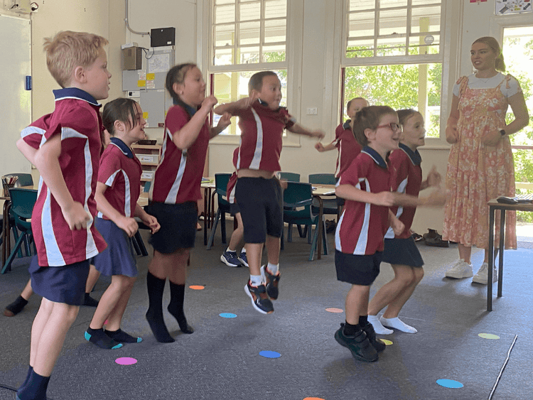A group of students smiling and jumping in a classroom with a teacher.