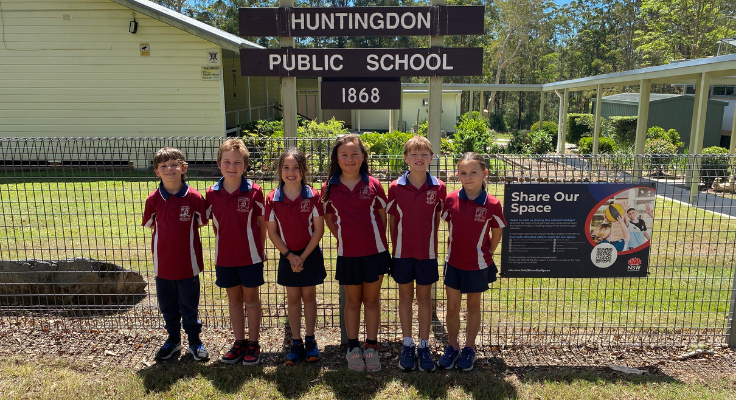 Smiling students standing in front of the Huntingdon Public School sign.