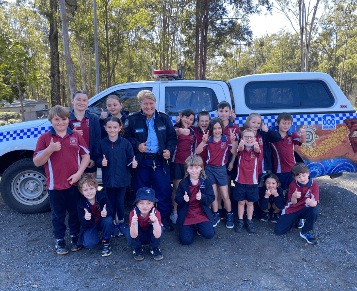 A group of students with a police officer standing next to a police vehicle.