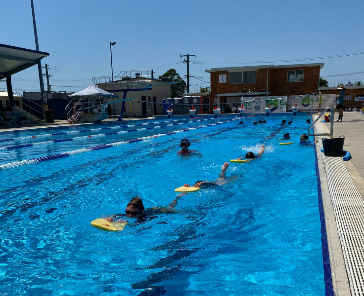 Students in a pool swimming with kickboards.
