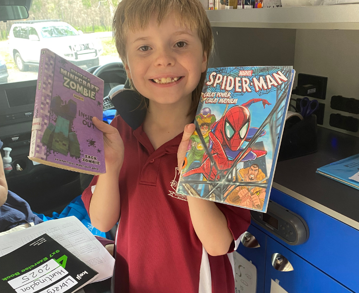 A student smiling holding a book in each hand.
