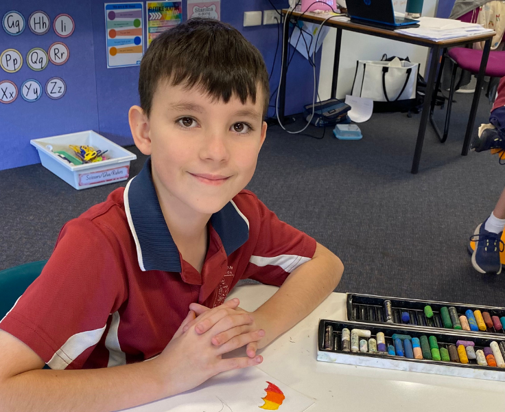A student sitting at a desk with paper and oil pastels.